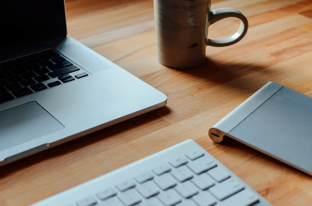 Laptop, keyboard and a mug on a wooden desk, seen from above while writing up a weekly report